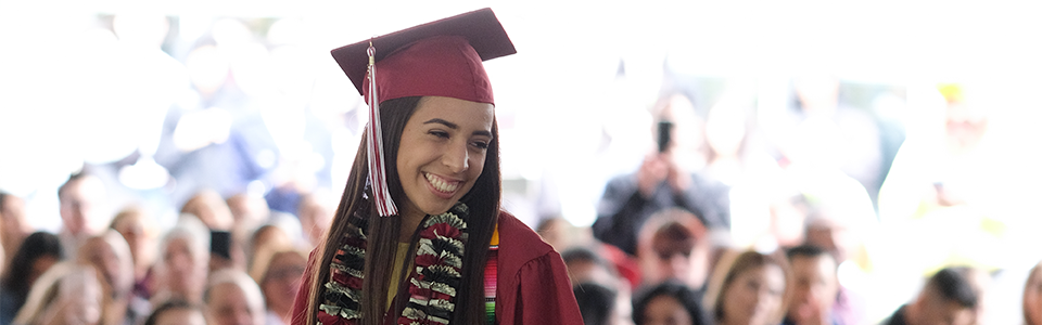 student pictured smiling at graduation, in front of a crowd