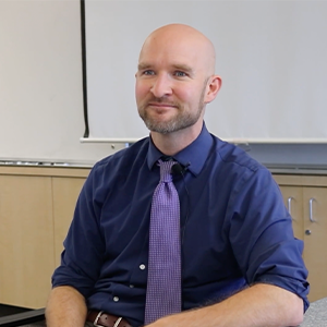 Teacher Cal Trembath sits in his classroom and smiles at the camera.